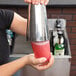 A person holding a Libbey tall mixing glass with a red drink in it.