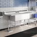 A stainless steel Advance Tabco three compartment sink with two drainboards.
