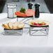 A table with a Tablecraft chrome metal riser set holding plates of bread, grapes, and butter.