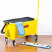 A Rubbermaid yellow mop pad on a Rubbermaid blue mop in a bucket on a wood floor.