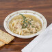 A Solo Symphony heavy weight paper bowl filled with soup, noodles, and a sprig of thyme.