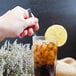 A hand holding a Walco iced tea spoon over a glass of ice tea with a lemon slice.