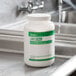 A white bottle with a green label of Noble Chemical Last Call Concentrated Low Suds Powdered Bar Glass Cleaner sitting on a sink.
