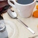 A cup of coffee with a Walco stainless steel demitasse spoon on a napkin next to it.