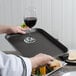 A person holding a Cambro non-skid serving tray with a glass of wine and a sandwich.