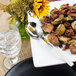 A plate of food with a Walco stainless steel serving spoon and a glass of water next to a flower.