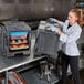 A woman in a white coat opening a grey Cambro food container with food inside.