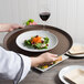 A person holding a Cambro Tavern Tan non-skid serving tray with a plate of salad, bread, and a glass of wine.