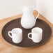 A white pitcher and two white mugs on a brown Cambro Treadlite non-skid tray.