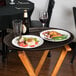 A Tavern Tan Cambro non-skid oval serving tray holding a plate of food, a glass of red wine, and a bottle of beer on a table.