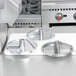 A Robot Coupe stainless steel food processor with three circular metal blades on a counter.