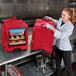 A woman in a white coat and gloves holding a red Cambro food container.