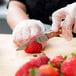 A person using a Mercer Praxis paring knife with a rosewood handle to cut a strawberry.