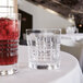 A glass of ice and a glass of red liquid on a table.