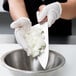 A person in gloves using a Mercer Culinary Praxis chef's knife to slice onions in a bowl.