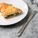 A Walco stainless steel table knife next to a piece of cheese and spinach pie on a plate.