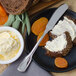 A close up of a Walco stainless steel butter spreader with white cream on a piece of bread.