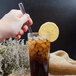 A hand using a Walco stainless steel iced tea spoon to stir a glass of iced tea with a lemon slice.