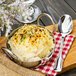 A Walco Luxor stainless steel teaspoon in a bowl of mashed potatoes on a wooden board.