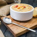 A Walco stainless steel bouillon spoon on a wooden surface next to a bowl of soup.