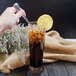 A hand holding a Walco Pacific Rim stainless steel iced tea spoon over a glass of iced tea with a lemon slice.