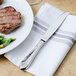 A Walco stainless steel table knife on a napkin next to a plate of meat and vegetables.