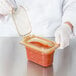 A gloved hand holding a Carlisle amber plastic container filled with red sauce.