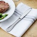 A Walco stainless steel dinner knife on a napkin next to a plate of steak and green beans.