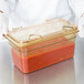 A person in gloves holding a Carlisle Amber High Heat hinged plastic lid on a container of red sauce.