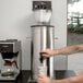 A man using a Bloomfield iced tea brewer to pour a drink into a cup.