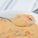 A Walco Meteor stainless steel large bowl bouillon spoon filled with soup over a white background.