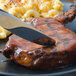 A Walco Bosa Nova stainless steel dinner knife cutting a piece of meat on a plate.