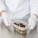 A person in white gloves holding a Carlisle clear plastic container of olives.