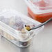 A Carlisle clear plastic food pan lid with olives and a black spoon in it.