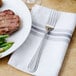 A Walco stainless steel table fork on a napkin next to a plate of food.