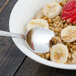 A bowl of oatmeal with bananas and strawberries with a Walco Saville teaspoon.