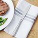 A Walco stainless steel dinner knife on a napkin next to a plate of steak and green beans.