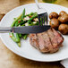 A Walco stainless steel dinner knife on a table with a plate of food and a fork.