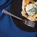 A Walco Bosa Nova stainless steel dinner fork on a plate with a pastry with a green leaf.