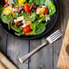 A plate of salad with a Walco Bosa Nova salad fork and bread on a table.