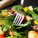 A Walco Bosa Nova stainless steel salad fork in the middle of a salad with vegetables.