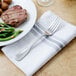 A Walco Saville European fork on a plate with steak, potatoes, and a napkin.