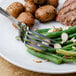 A plate of food with a Walco Saville European fork next to green beans and potatoes.