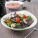 A Villeroy & Boch white porcelain deep bowl filled with salad with tomatoes and mushrooms.