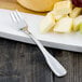 A Walco Saville stainless steel cocktail fork on a plate of cheese and grapes.