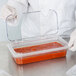 A person in gloves holding a Carlisle clear polycarbonate hinged lid over a container of red sauce.