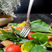 A Walco stainless steel salad fork on a plate of salad with vegetables.
