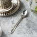 A Walco stainless steel demitasse spoon on a table next to a glass of water.