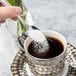 A Walco Marcie demitasse spoon pouring sugar into a cup of coffee.