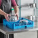 A man in an apron holding a blue Carlisle dish rack with clear glass bowls inside.